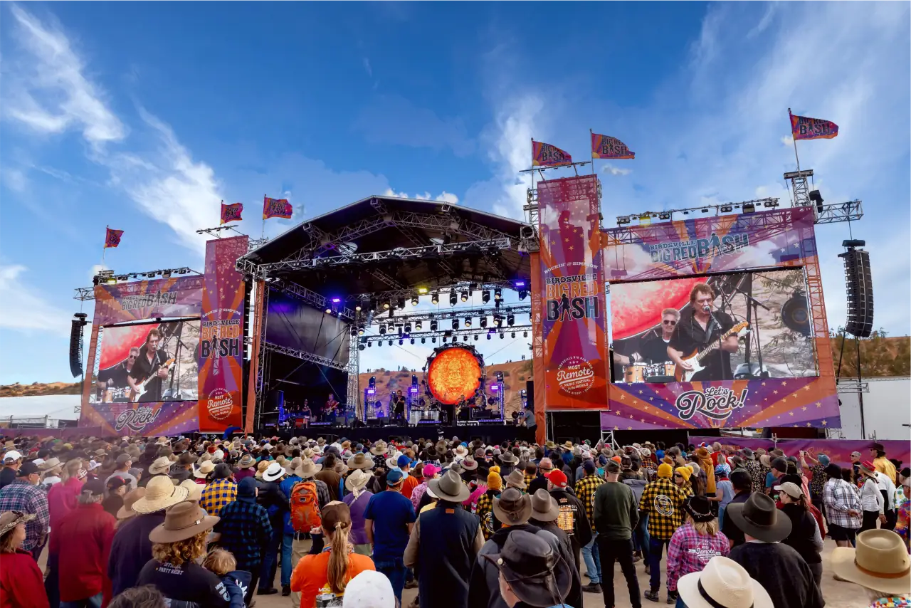 A festival main stage under a blue sky, with a crowd in front of it