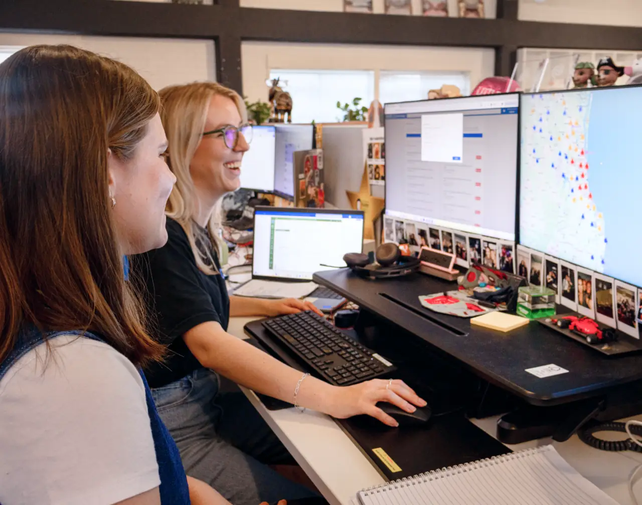 Two team members working together at a desk with large monitors