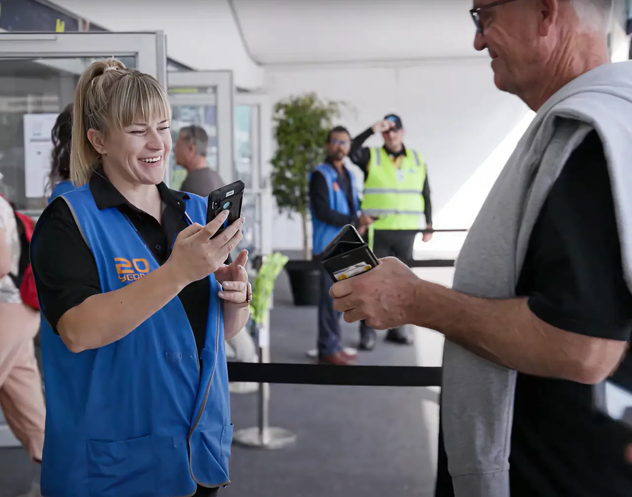 A staff member in a blue vest scanning a ticket on a phone at an event entry