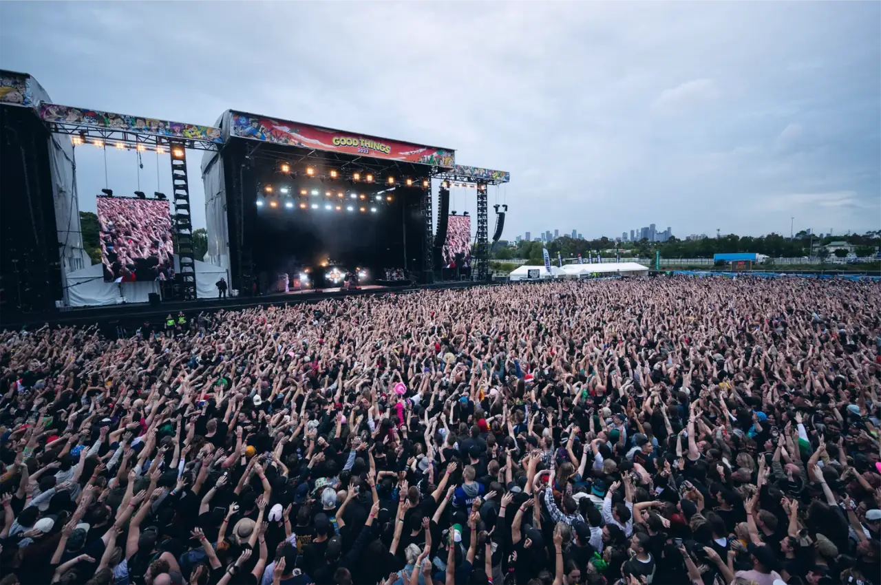 A huge festival crowd facing a main stage, seen from above