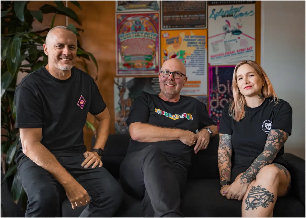 Three people sitting together on a couch in a bar lined with gig posters